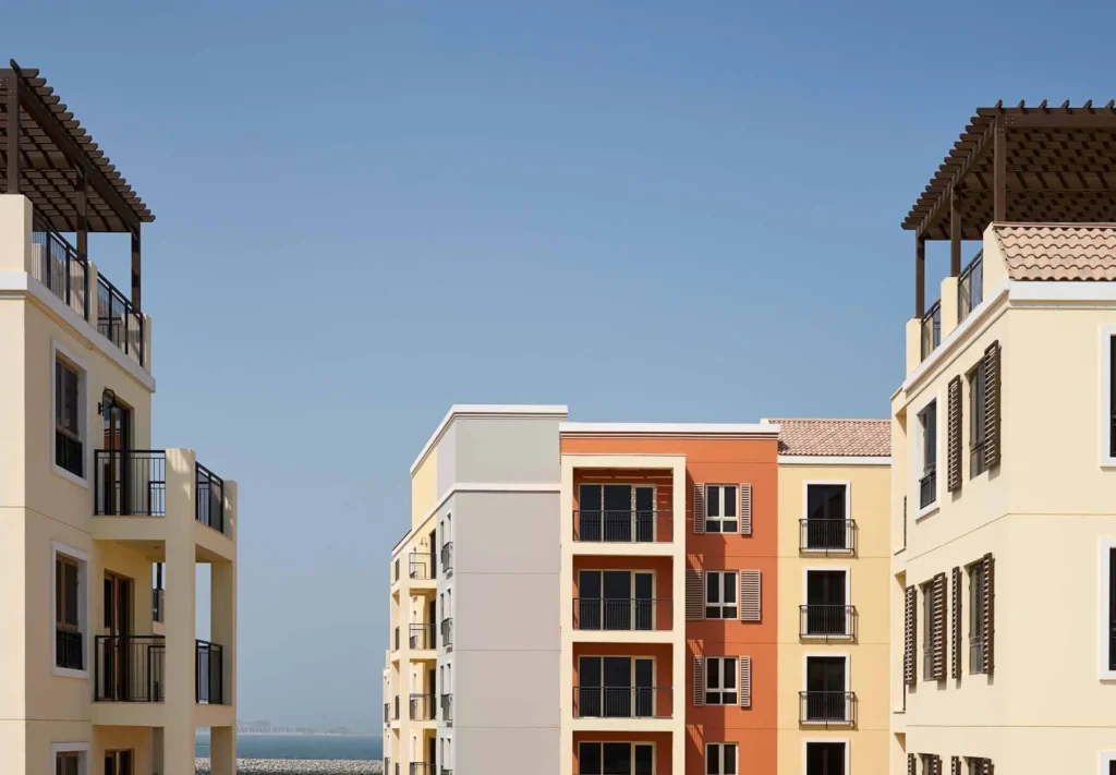 Pastel-coloured Port de La Mer apartment buildings with balconies against a blue sky (developer rendering)