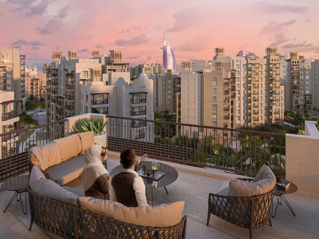 Terrace of an Al Jazi apartment with lounge seating and views toward Burj Al Arab at sunset (developer rendering)