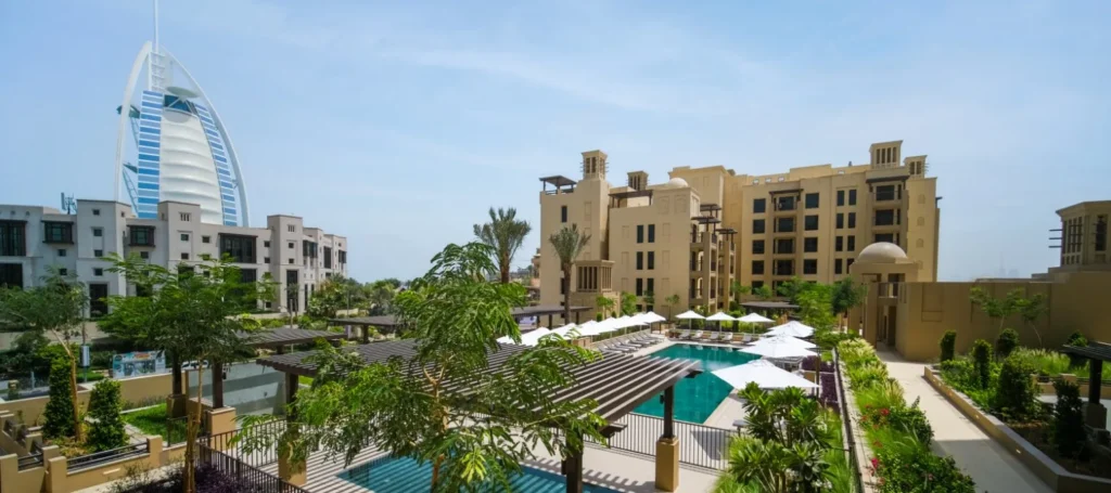 Lamtara pool courtyard with palms and Burj Al Arab visible beyond the buildings (developer rendering)