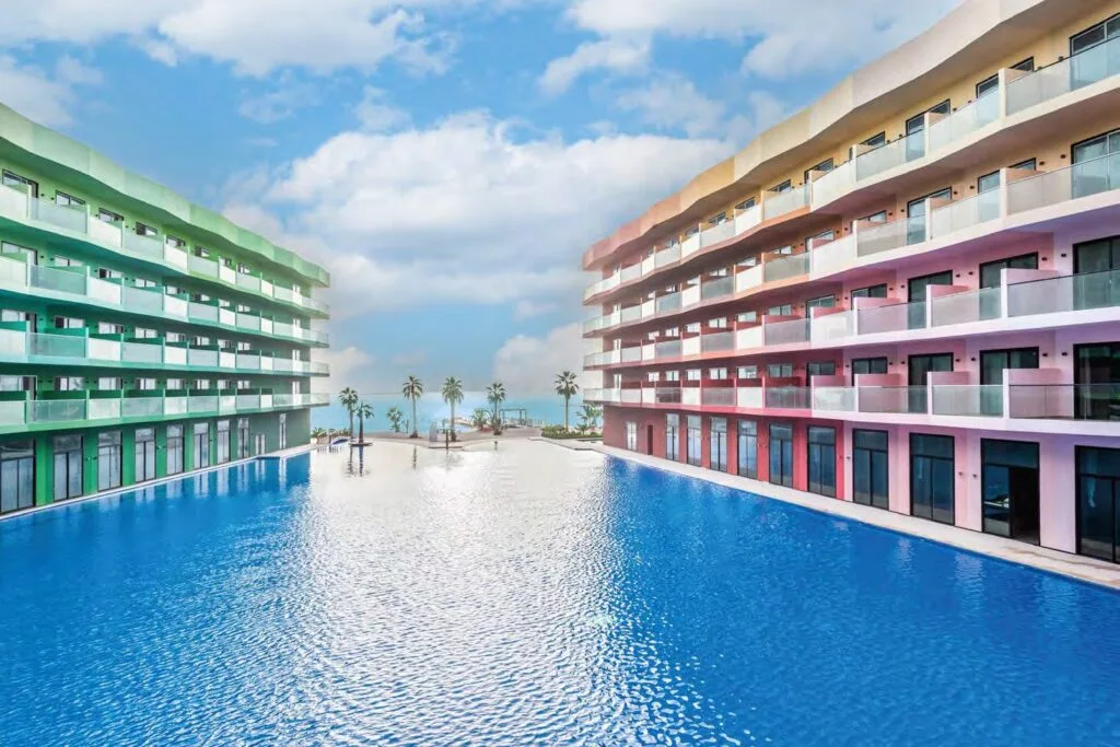 Two modern buildings flanking a large swimming pool with palm trees
