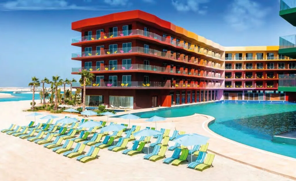 Exterior view of colorful building with pool and beach chairs