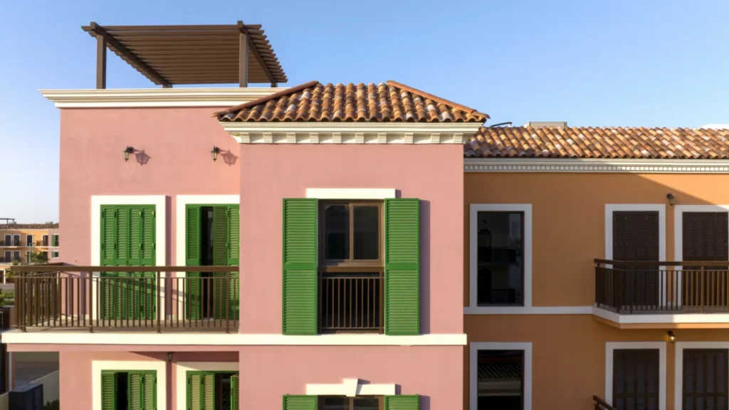 Close-up of a pink Sur La Mer townhouse with green shutters, balcony and terracotta roof