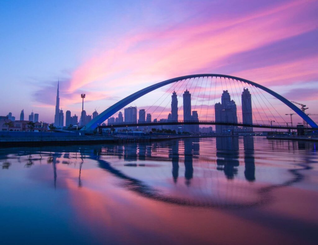 Arch bridge over water with Dubai skyline at sunset