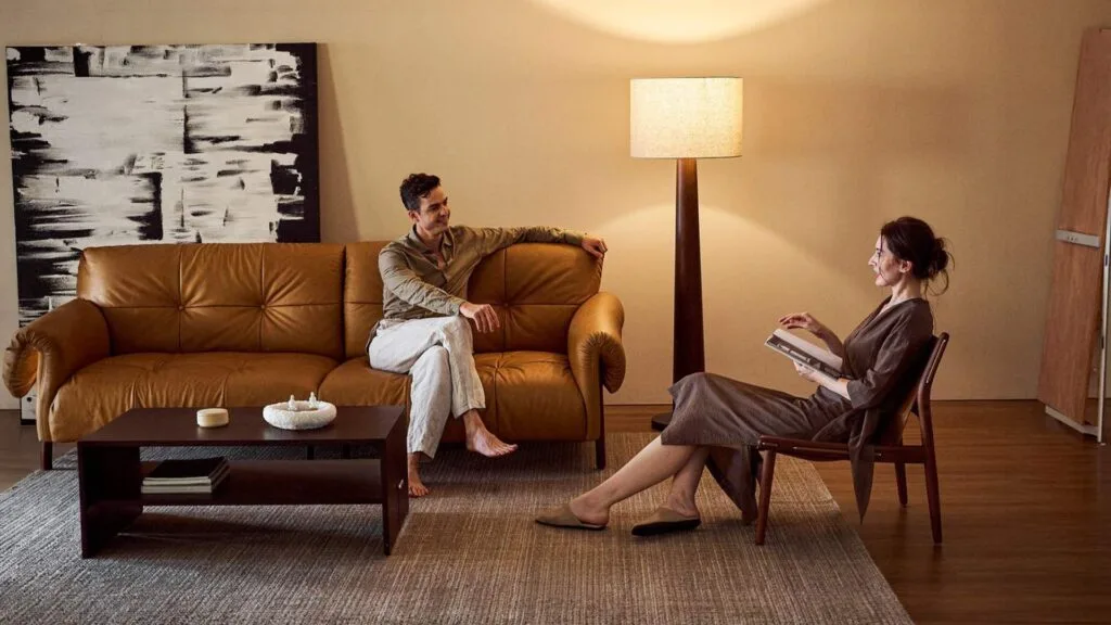 Interior living room with brown sofa, wooden chair, and floor lamp